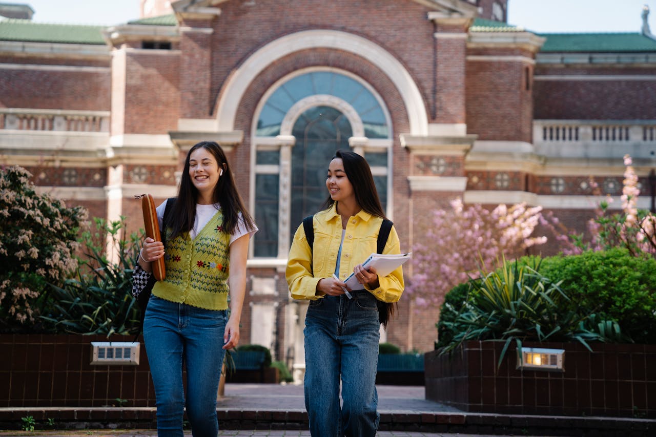Two smiling young women walk together on a beautiful college campus.